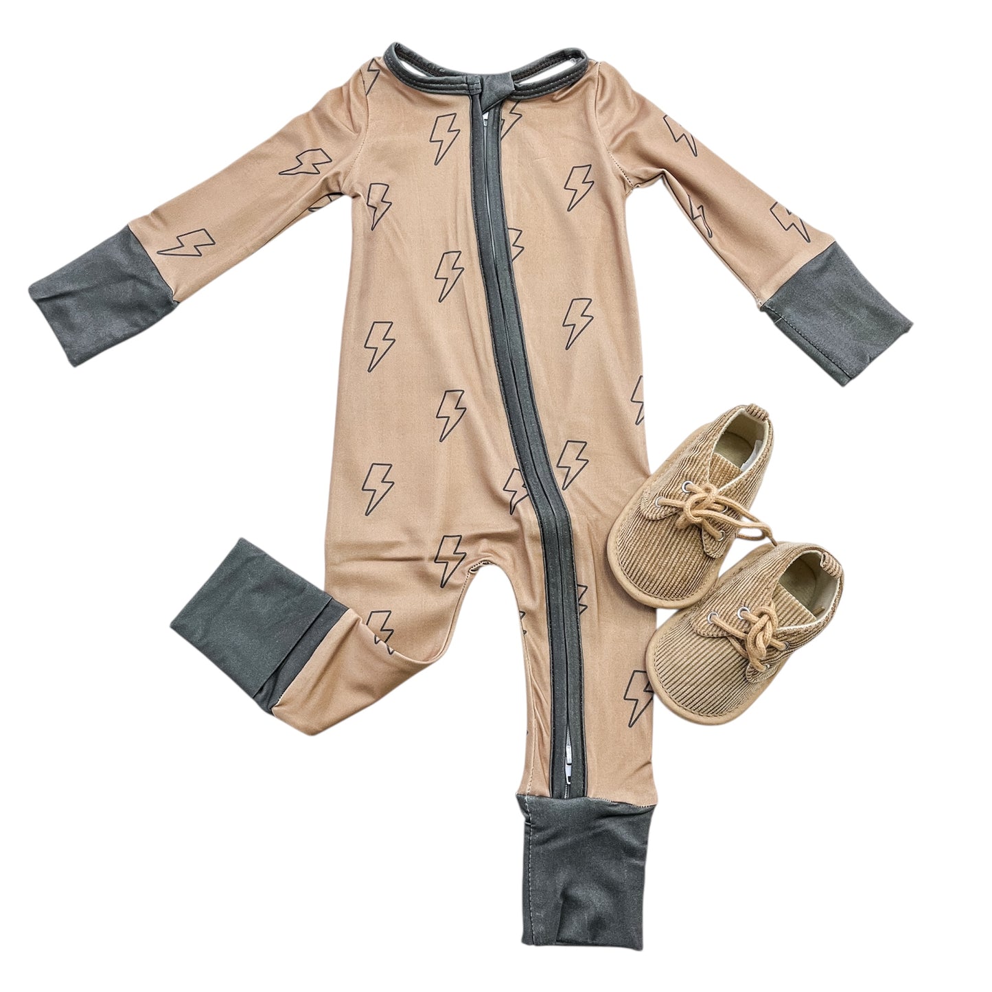 The Thunderbolt Zippy by Tiny Tot Bundles is a tan baby onesie with black lightning bolt patterns, dark gray cuffs, and a black zipper, shown flat beside matching tan baby moccasins with laces.