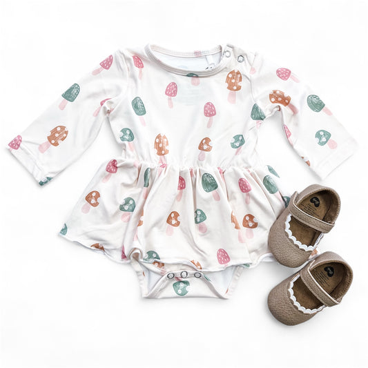 The Mushroom Meadow Longsleeve Twirl Romper by Tiny Tot Bundles, featuring colorful mushroom prints, is paired with brown baby shoes and displayed flat on a white background.
