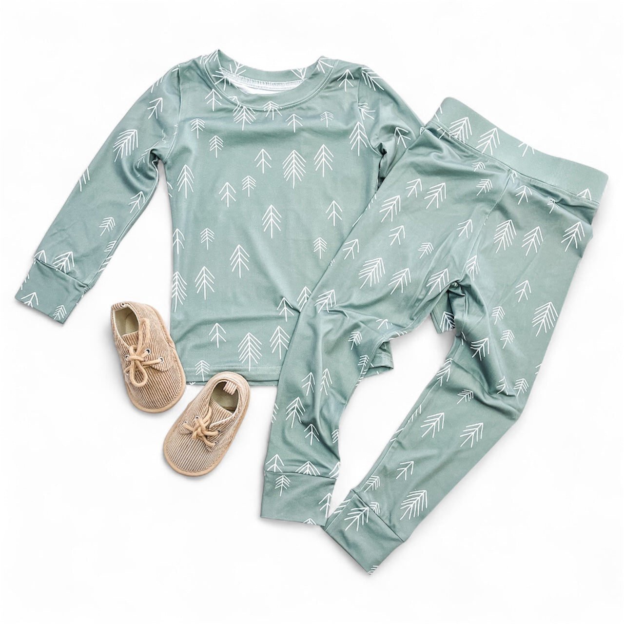 The Mini Timber Jammies Set by Tiny Tot Bundles includes a green top and matching pants with white tree patterns, paired with light brown baby shoes, all displayed on a white background.