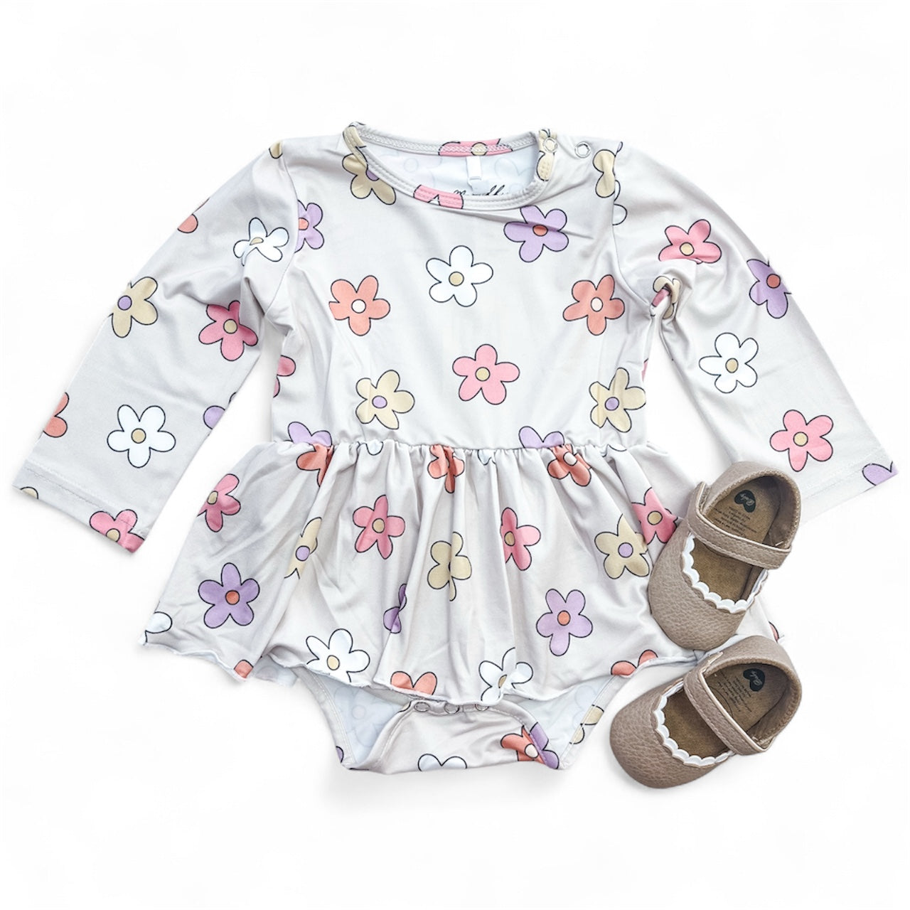 The Tiny Tot Bundles Groovy Garden Longsleeve Twirl Romper, featuring a pastel flower pattern and ruffled skirt, is paired with brown baby shoes with white scalloped trim, all shown on a white background.