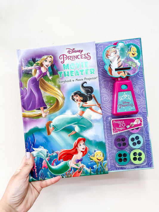 A hand holds the Disney Princess Movie Theater Book by Simon & Schuster, featuring characters like Rapunzel, Ariel, Sebastian, Flounder, a pink projector, and four image reels attached to the book’s right side.