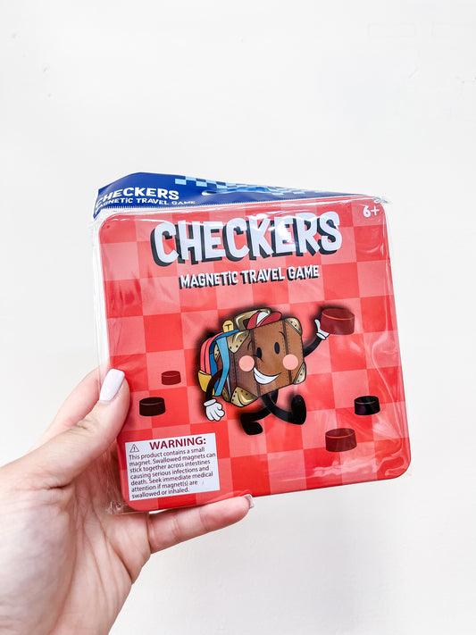 A hand holds a red Toy Smith Magnetic Travel Game - Checkers tin, featuring a cartoon checker piece and a warning label in the bottom left corner. The game is recommended for ages 6 and up.
