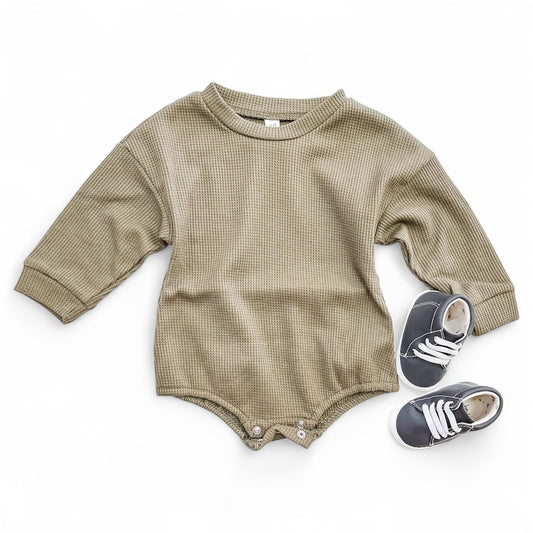 The Sage Wood Bubble by Tiny Tot Bundles, a beige long-sleeve baby romper with bottom snaps, is laid flat beside small gray baby sneakers with white laces on a white background.