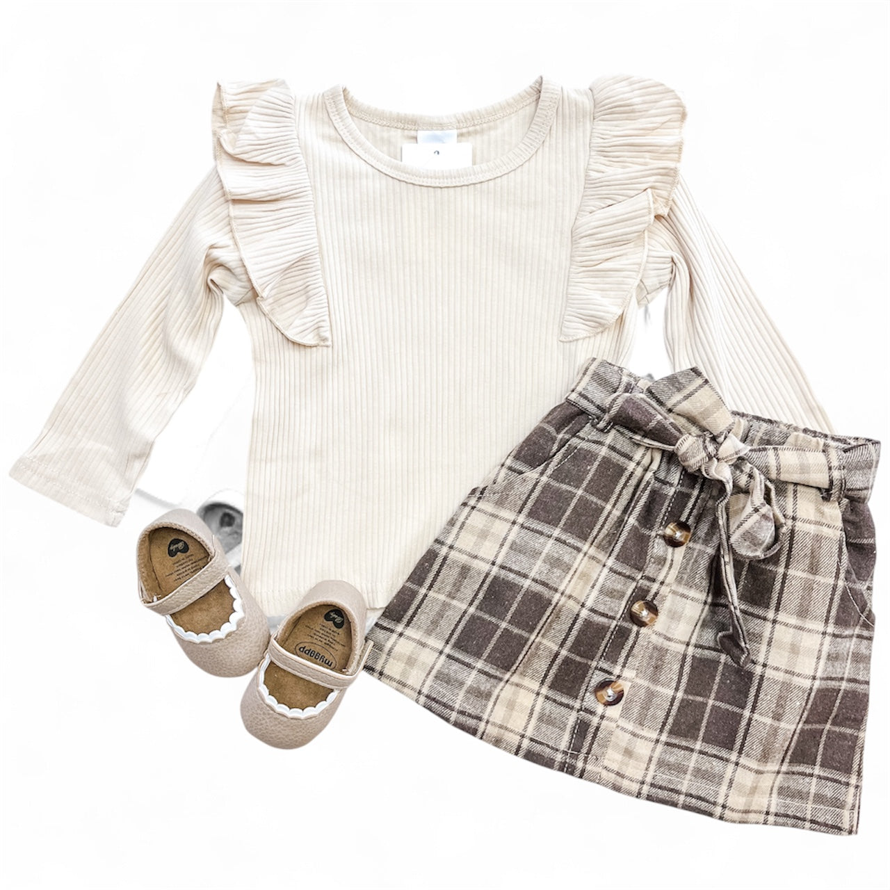 The Tiny Tot Bundles Autumn Days Skirt Set includes a cream ruffled long-sleeve top, a brown plaid skirt with a bow and buttons, and beige scalloped-edge shoes for toddler girls.