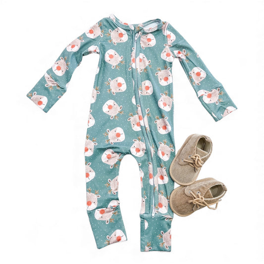The Tiny Tot Bundles Rudolph Dreams Zippy, a green baby onesie with reindeer print and a front zipper, is laid flat beside tan corduroy baby shoes with bows, all displayed on a white background.