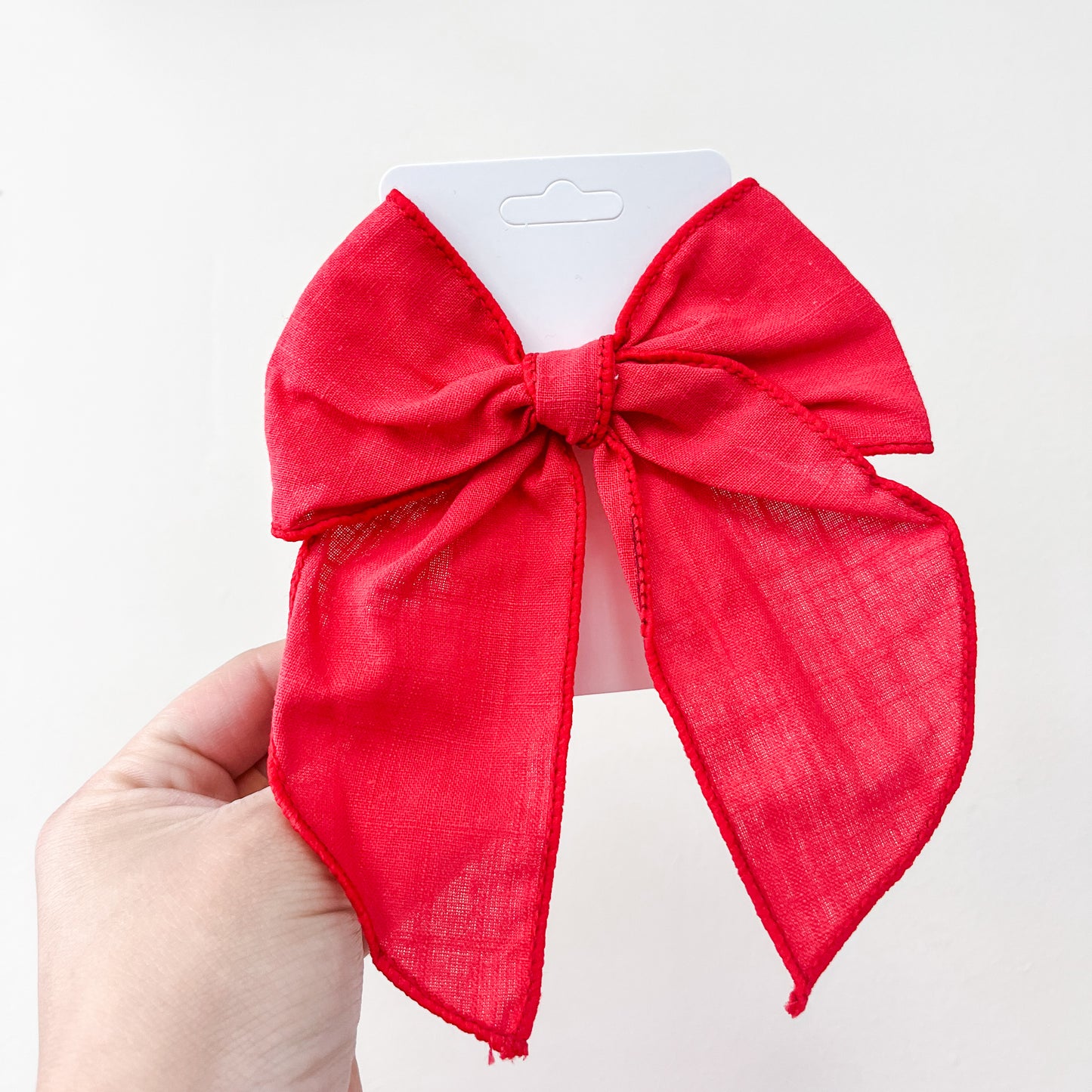 A hand holds a red fabric bow from the Tiny Tot Bundles Holiday Cheer Bow Set, displayed on a white card against a plain white background.