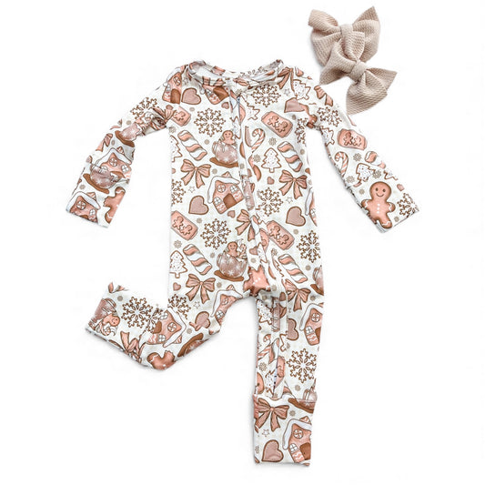 The Gingerbread Dreams Zippy by Tiny Tot Bundles, a festive onesie with gingerbread and candy print, is displayed flat beside a beige knit bow headband on a white background.