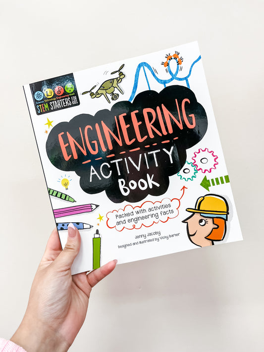 A hand holds the Stem Starters Art Activity Book: Engineering by Simon & Schuster, featuring colorful illustrations of gears, tools, circuits, and a person in a hard hat on the cover. The book offers activities and engineering facts.