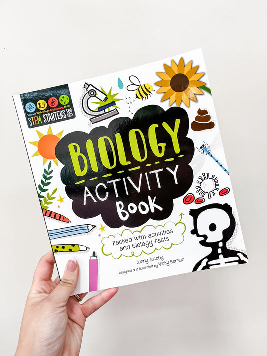 A hand holds the Simon & Schuster Stem Starters Art Activity Book: Biology, featuring colorful cover illustrations like a sunflower, microscope, skeleton, pencil, leaf, and beaker. Designed for kids, it includes STEM activities and facts.