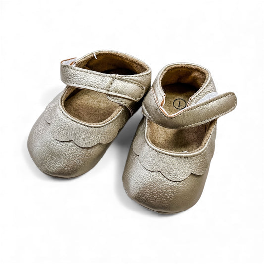 The Golden Petal Mary Jane by Tiny Tot Bundles: a pair of small, metallic gold baby shoes with scalloped edges and Velcro straps, displayed on a white background.