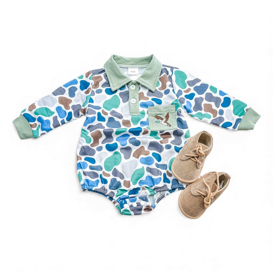 The Mallard Meadow Bubble by Tiny Tot Bundles features a blue, green, and brown camo baby romper with green collar and cuffs, a bird patch on the chest, and tan baby shoes, all shown on a white background.