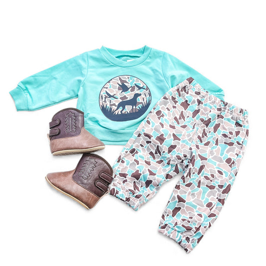 The Wild Tracks Outfit Set by Tiny Tot Bundles includes a teal long-sleeve wildlife graphic shirt, matching camo pants, and brown Western-stitched boots for toddlers.