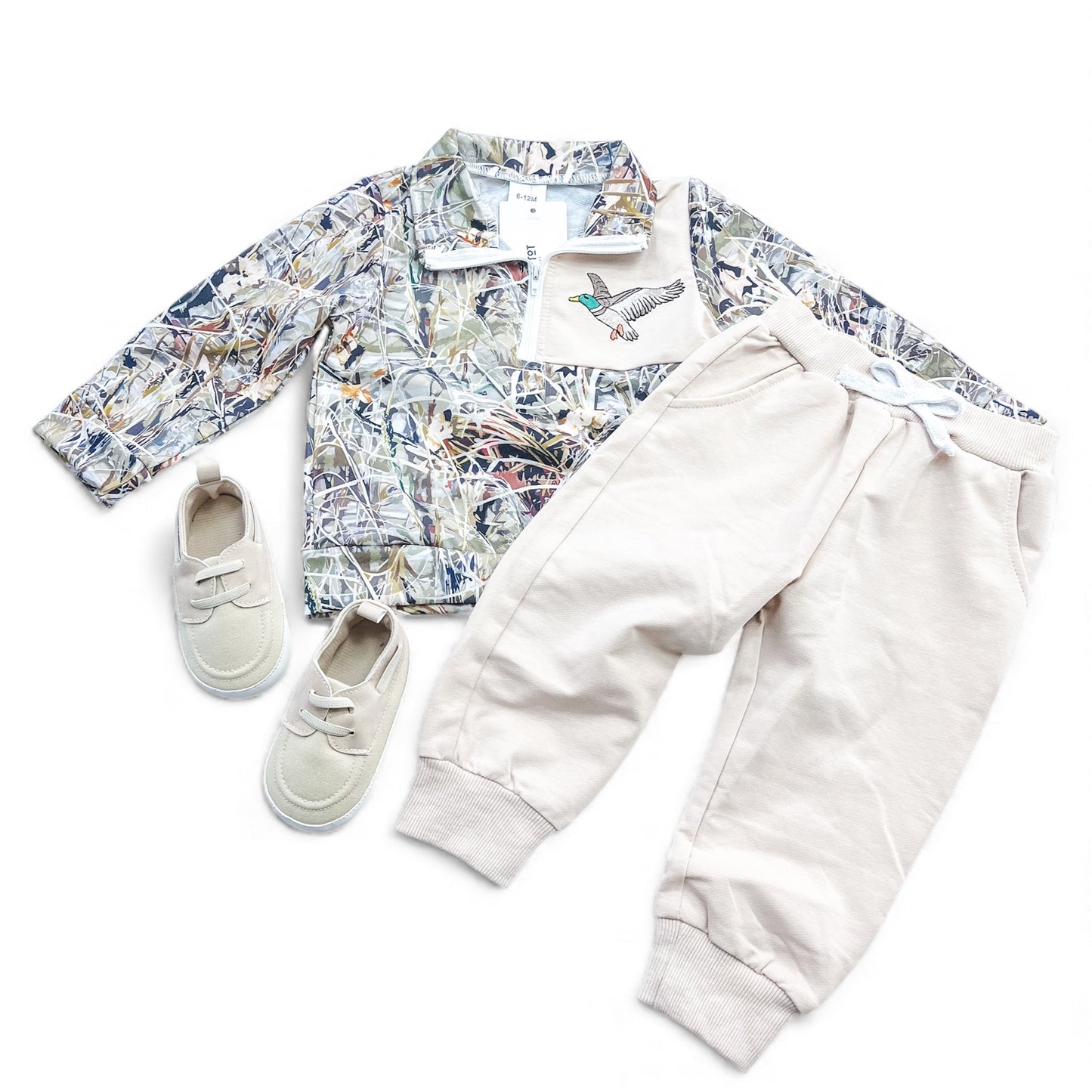 The Duck Trails Set by Tiny Tot Bundles includes a camo jacket with a bird patch, cream jogger pants with drawstring waist, and matching cream slip-on shoes, arranged flat on a white background.