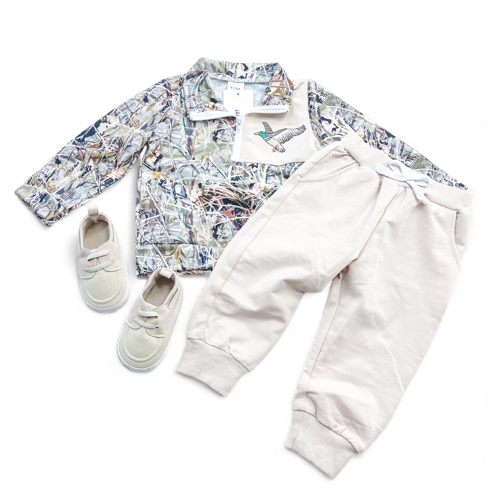 The Duck Trails Set by Tiny Tot Bundles includes a camo jacket with a bird patch, cream jogger pants with drawstring waist, and matching cream slip-on shoes, arranged flat on a white background.