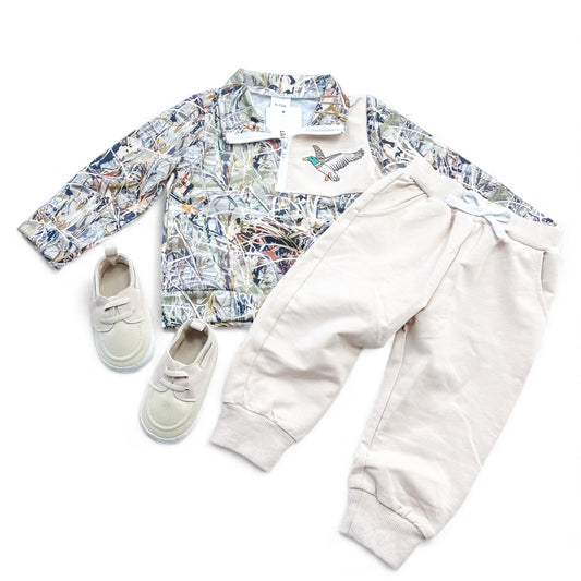 The Duck Trails Set by Tiny Tot Bundles includes a camo jacket with a bird patch, cream jogger pants with drawstring waist, and matching cream slip-on shoes, arranged flat on a white background.