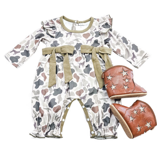 The Camouflage Cutie Ruffle Romper by Tiny Tot Bundles features long sleeves, green trim, ruffles, and bows in a camo-print, paired with brown baby boots accented by silver star patches.