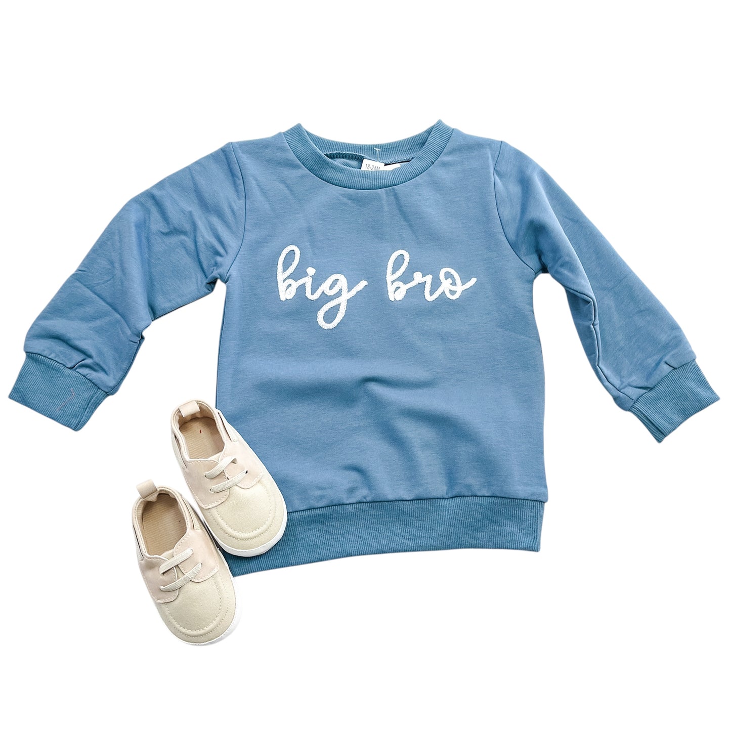 The Tiny Tot Bundles Big Bro Pullover, a blue sweatshirt with "big bro" in white letters, is shown alongside small beige toddler shoes on a white background.