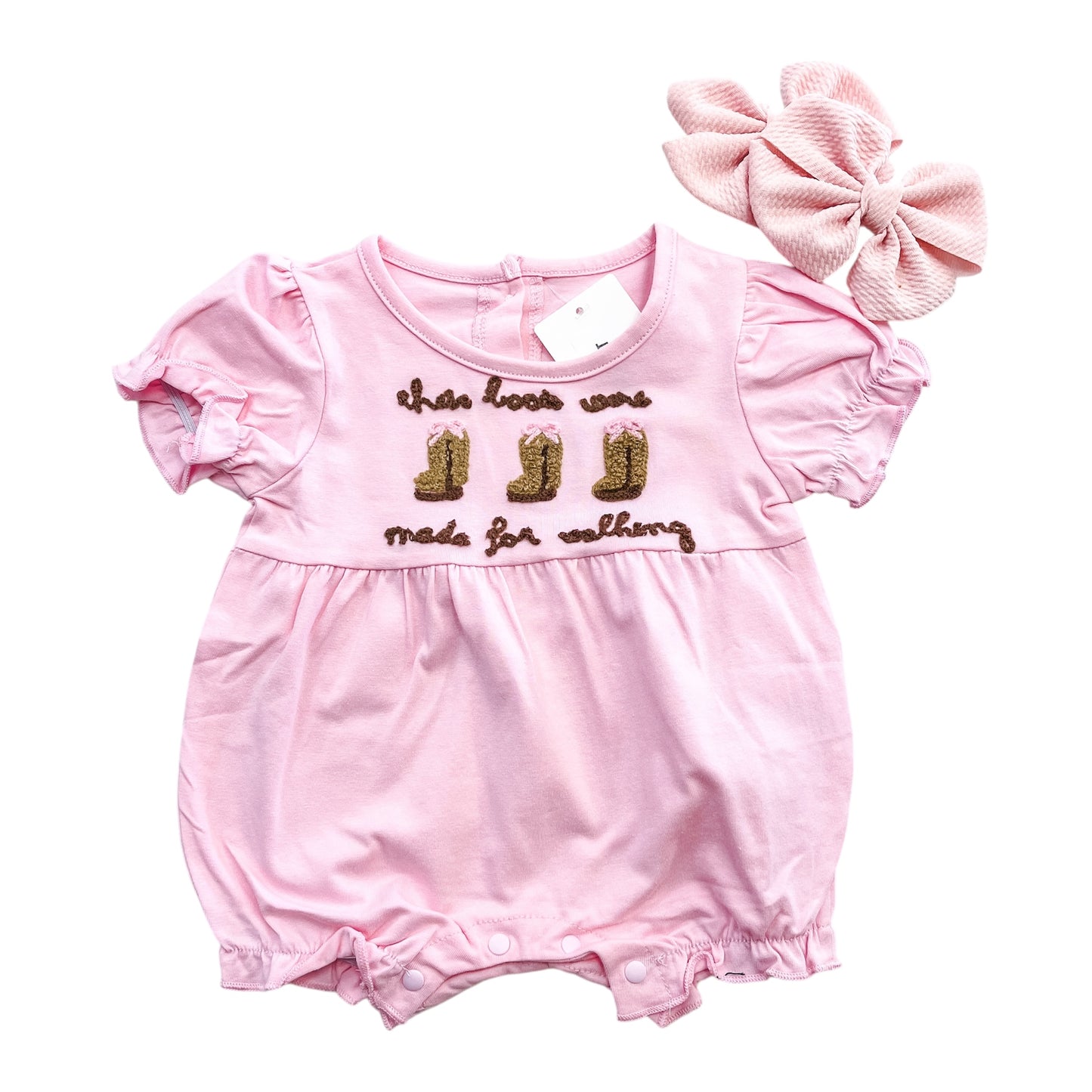 The Boot Scootin' Bubble by Tiny Tot Bundles features a pink baby romper with puff sleeves, ruffled legs, gold embroidered boots and 'these boots were made for walking' text, plus a matching textured headband with large bow.