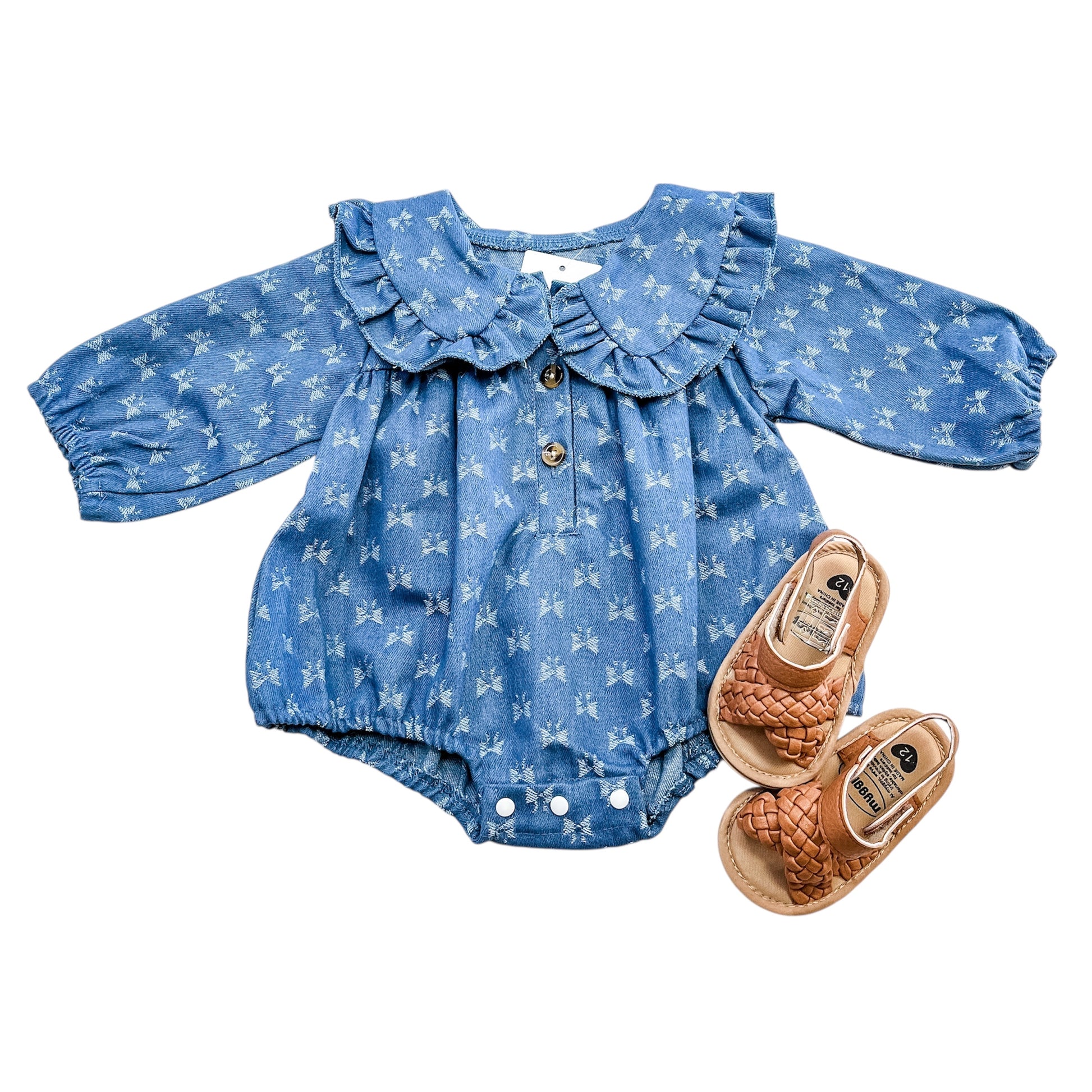 The Tiny Tot Bundles Starry Blue Belle Bubble features long sleeves, a ruffled collar, and white star patterns, paired with tan woven baby sandals.