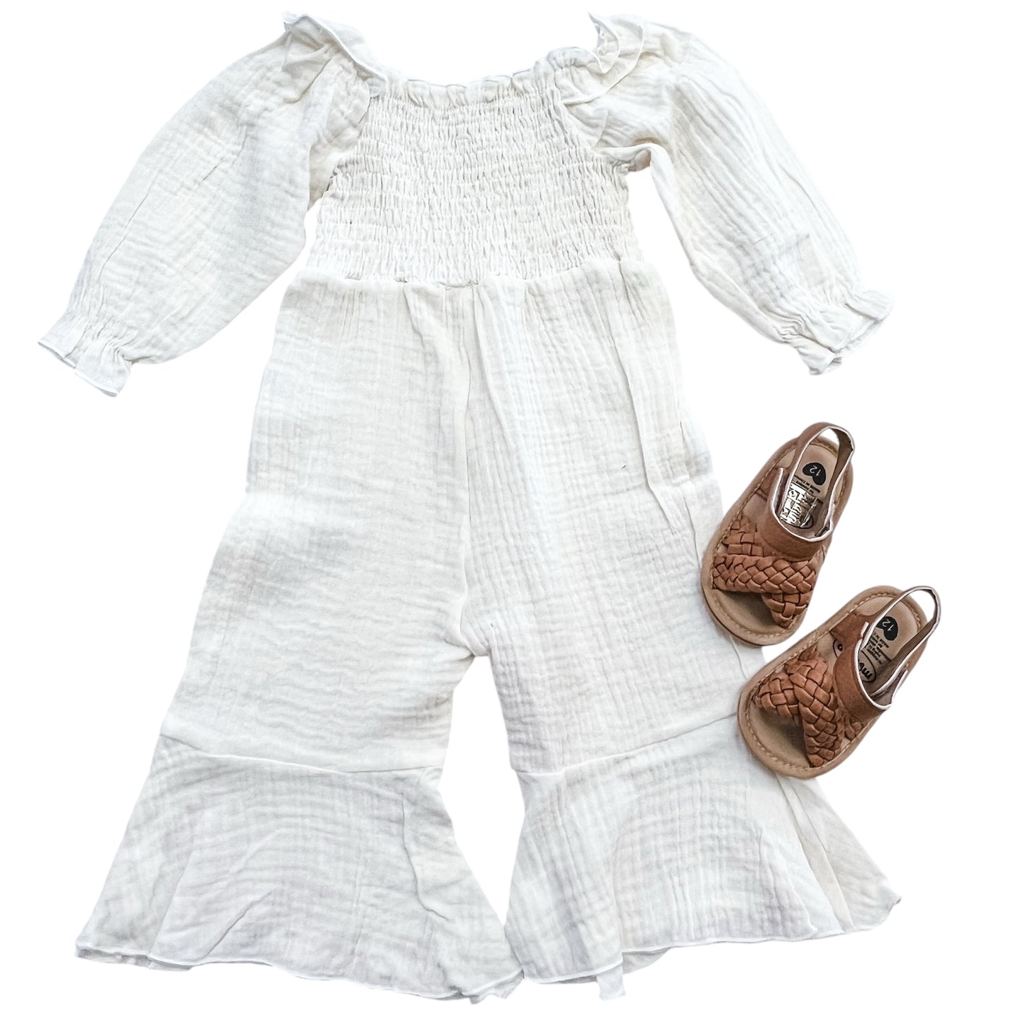 The Tiny Tot Bundles Ivory Meadow Smocked Romper is displayed beside brown woven ankle-strap sandals, all set on a white background.