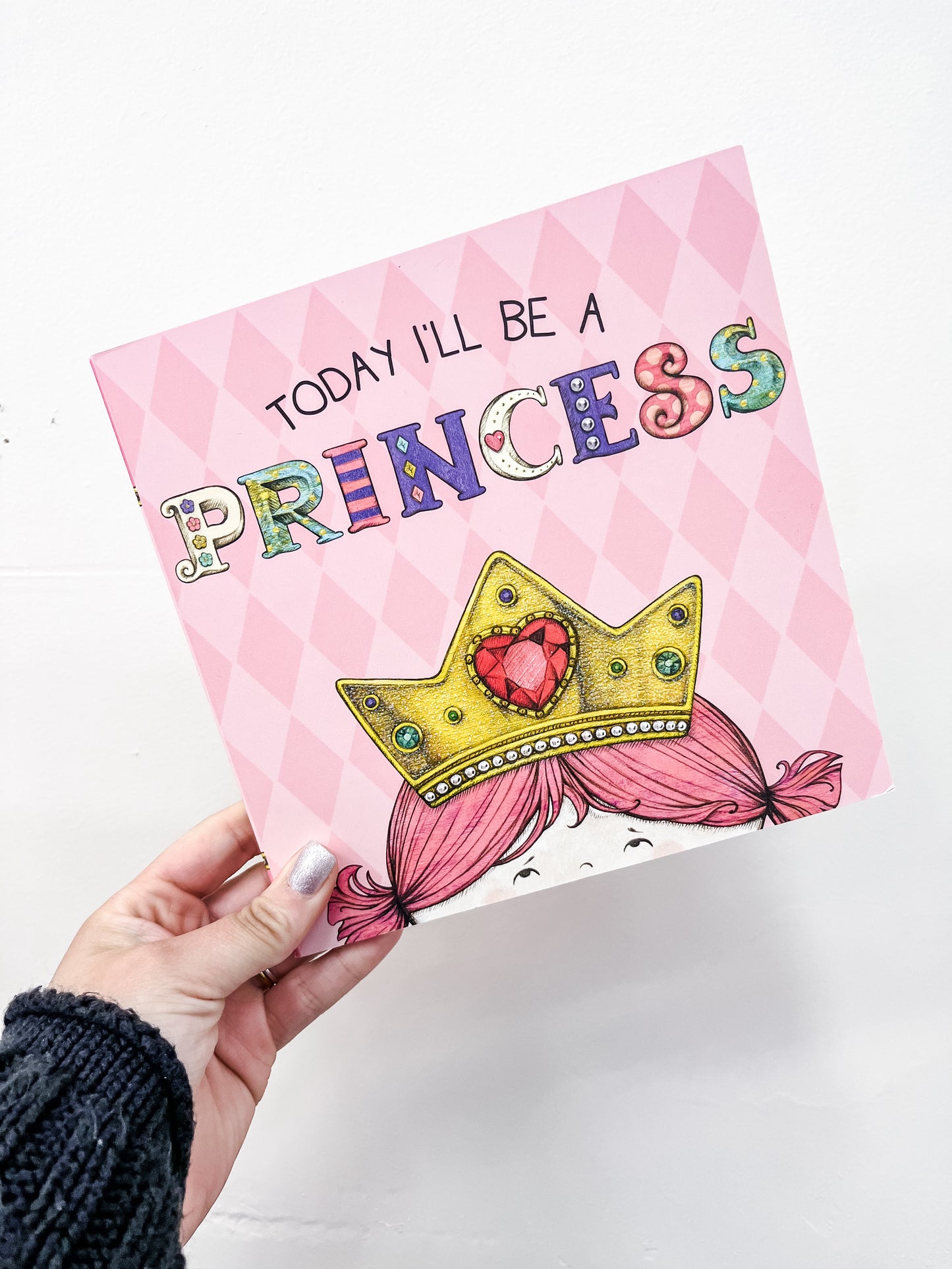 A hand holds the Tiny Tot Bundles "Today I'll Be A Princess Book," featuring a cartoon crown and a girl with pink pigtails on the cover.