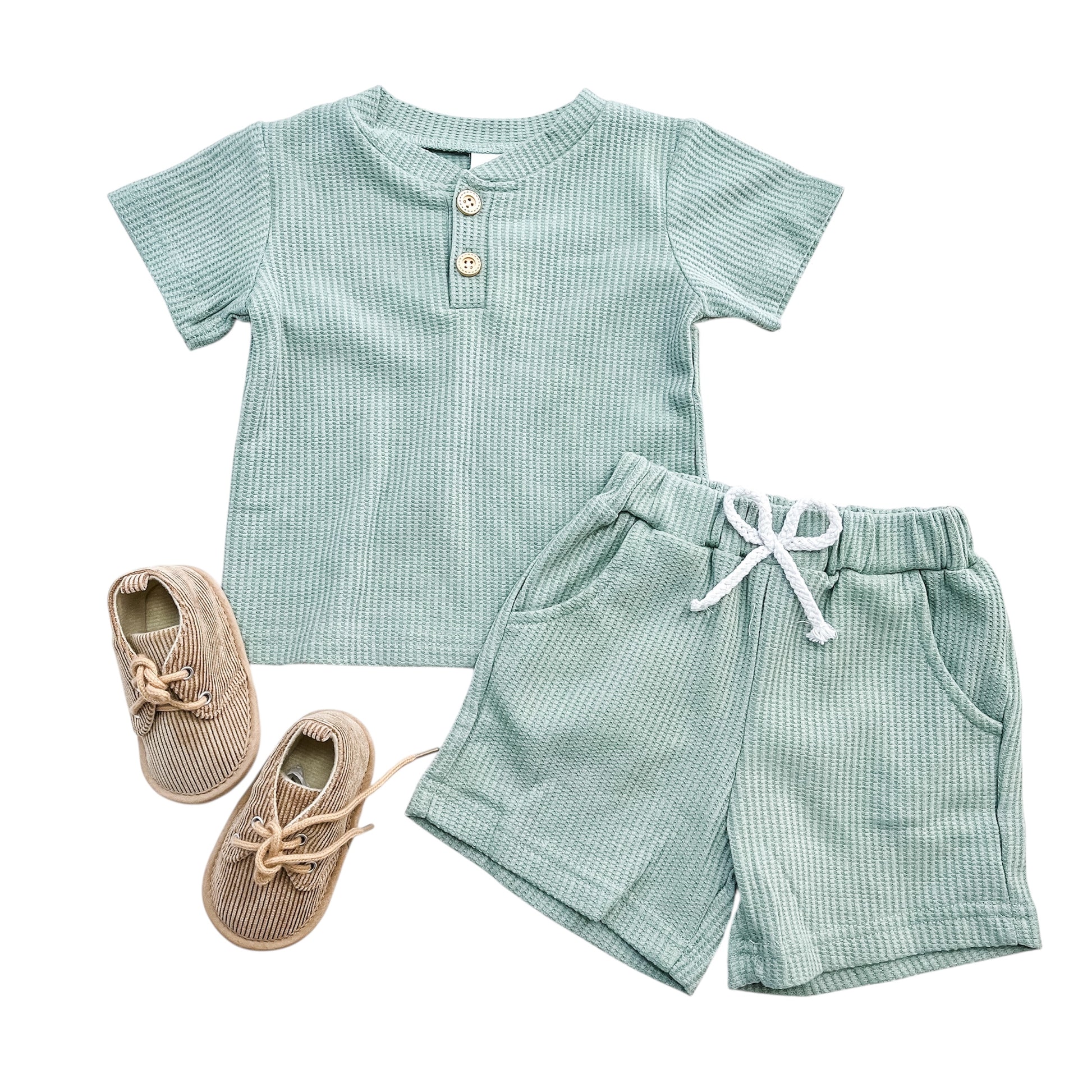 The Essentials Boys Set by Tiny Tot Bundles features a mint green short-sleeve shirt with buttons, matching shorts with a white drawstring, and beige lace-up baby shoes, all displayed on a white background.