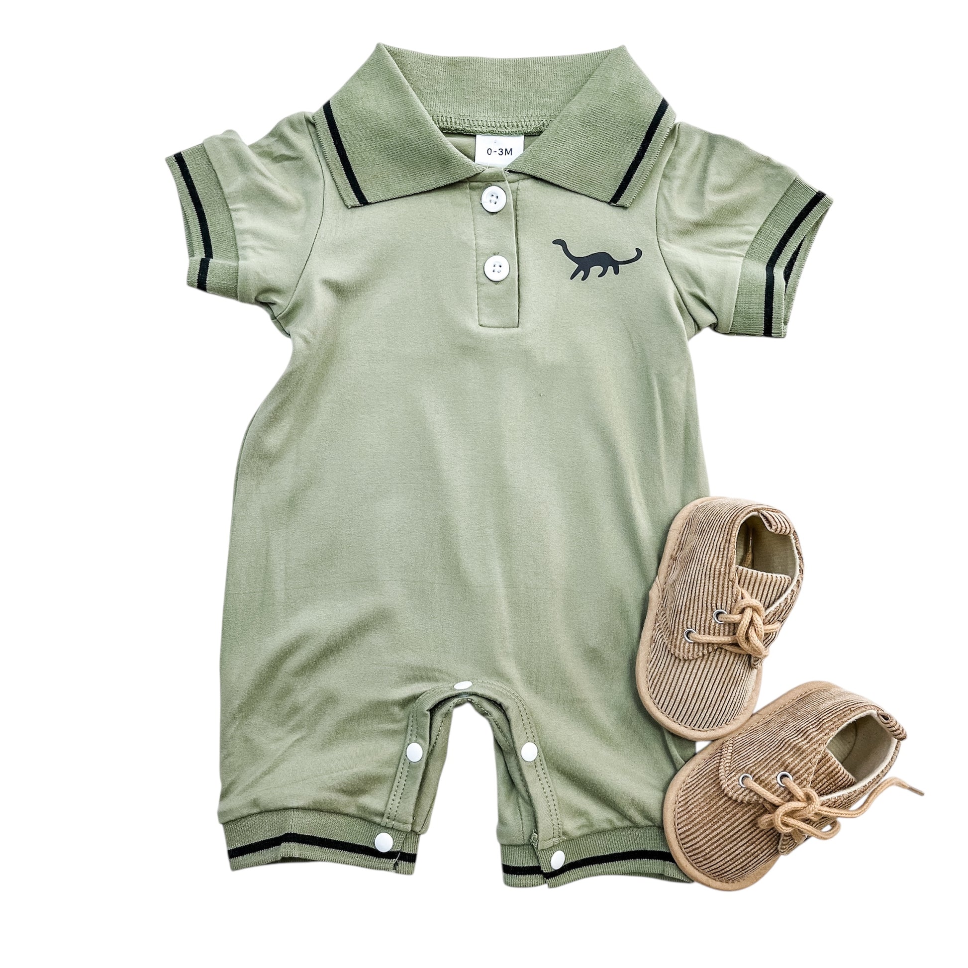 The Little Dino Polo Romper by Tiny Tot Bundles is a light green baby outfit with short sleeves, black trim, buttons, and a small dinosaur graphic, shown with tan corduroy baby shoes with laces on a white background.