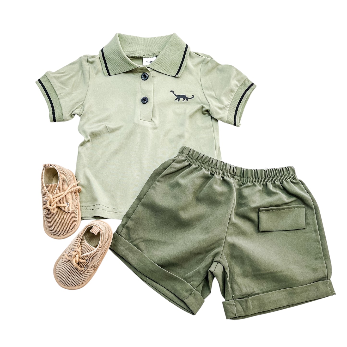 The Little Dino Polo Set by Tiny Tot Bundles features a light green short-sleeve polo with a dinosaur graphic, matching green shorts with a back pocket, and tan lace-up baby shoes, all displayed on a white background.