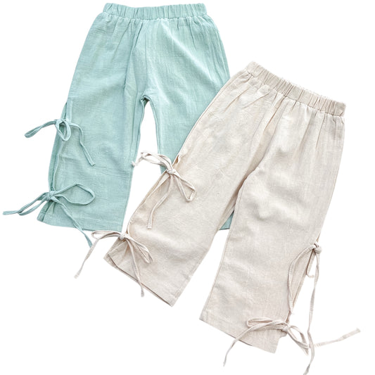 Two pairs of Tiny Tot Bundles Linen Side-Bow Everyday Pants—one light blue, one beige—with elastic waists and decorative calf ties, displayed on a white background.