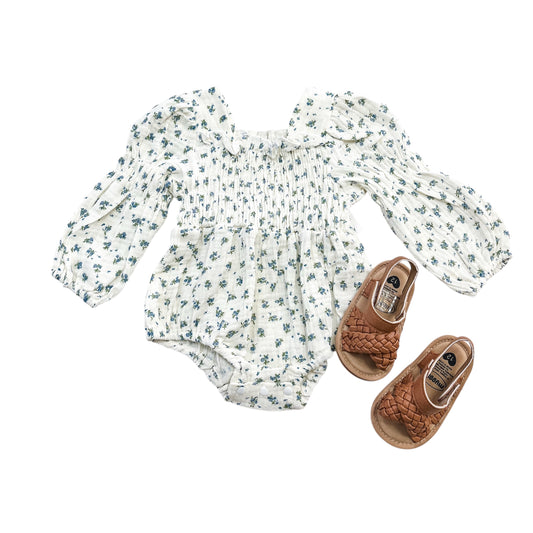 The Vintage Blue Scrunch Romper + Bow by Tiny Tot Bundles is displayed with brown woven baby sandals, all arranged neatly on a white background.