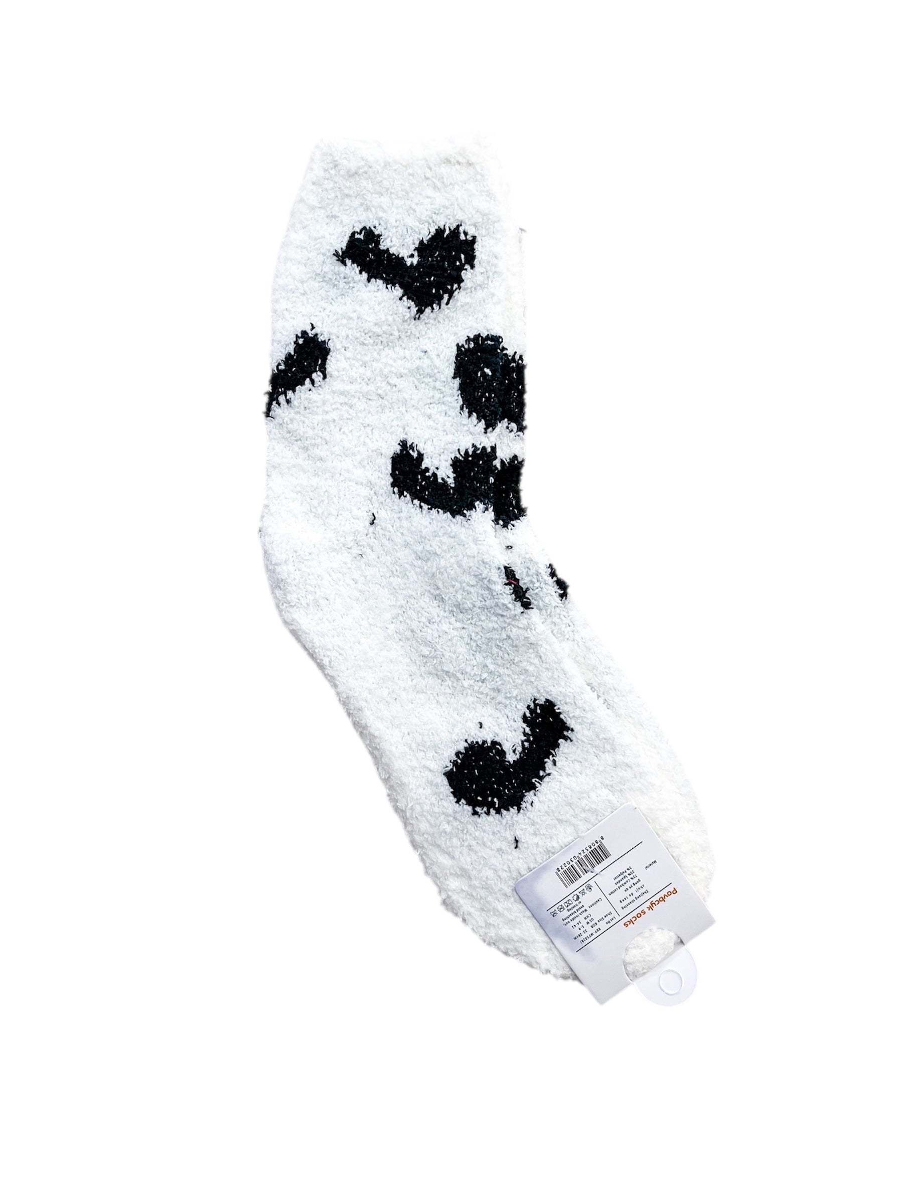 The love & repeat Sweetheart Lounge Sock, featuring white fuzzy fabric with black heart-shaped spots, is shown on a white background with an attached retail tag displaying a barcode and product details.