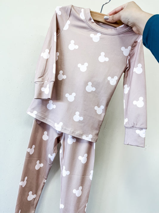 A hand holds up the Cozy Mouse Jammies Set by Tiny Tot Bundles—a matching light pink children’s pajama set with long sleeves and pants, featuring a white Mickey Mouse head pattern.