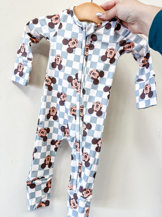 A hand holds Tiny Tot Bundles’ Classic Mouse Checkered Zippy: a baby onesie on a wooden hanger, featuring a blue and white checkered pattern with repeated cartoon mouse faces.