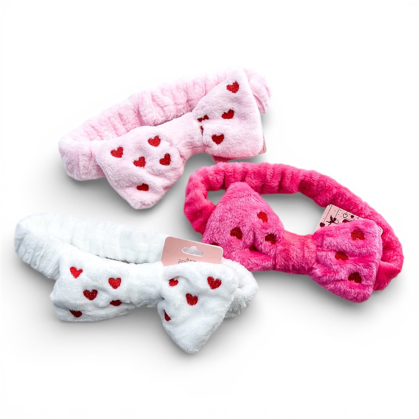 The love & repeat Sweetheart Plush Bow Headwraps set includes three fluffy headbands in pink, hot pink, and white, each with a matching bow and small red heart patterns, displayed on a white background.