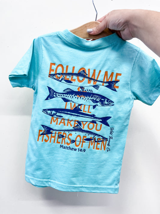 A hand holds the Wild Threads Co "Follow Me T-Shirt," a light blue children's tee featuring blue fish and orange text: “FOLLOW ME & I WILL MAKE YOU FISHERS OF MEN” with Matthew 14:9.