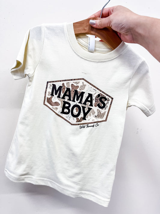 A hand displays the cream-colored Mama's Boy Camo T-Shirt by Wild Threads Co, featuring a hexagonal “MAMA’S BOY” patch with a camouflage background.