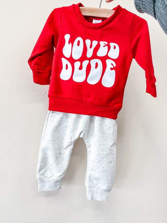 The Loved Dude Lounge Set by Tiny Tot Bundles features a red long-sleeve top with "LOVED DUDE" in bold white letters and light gray pants, both displayed on a hanger against a plain background.
