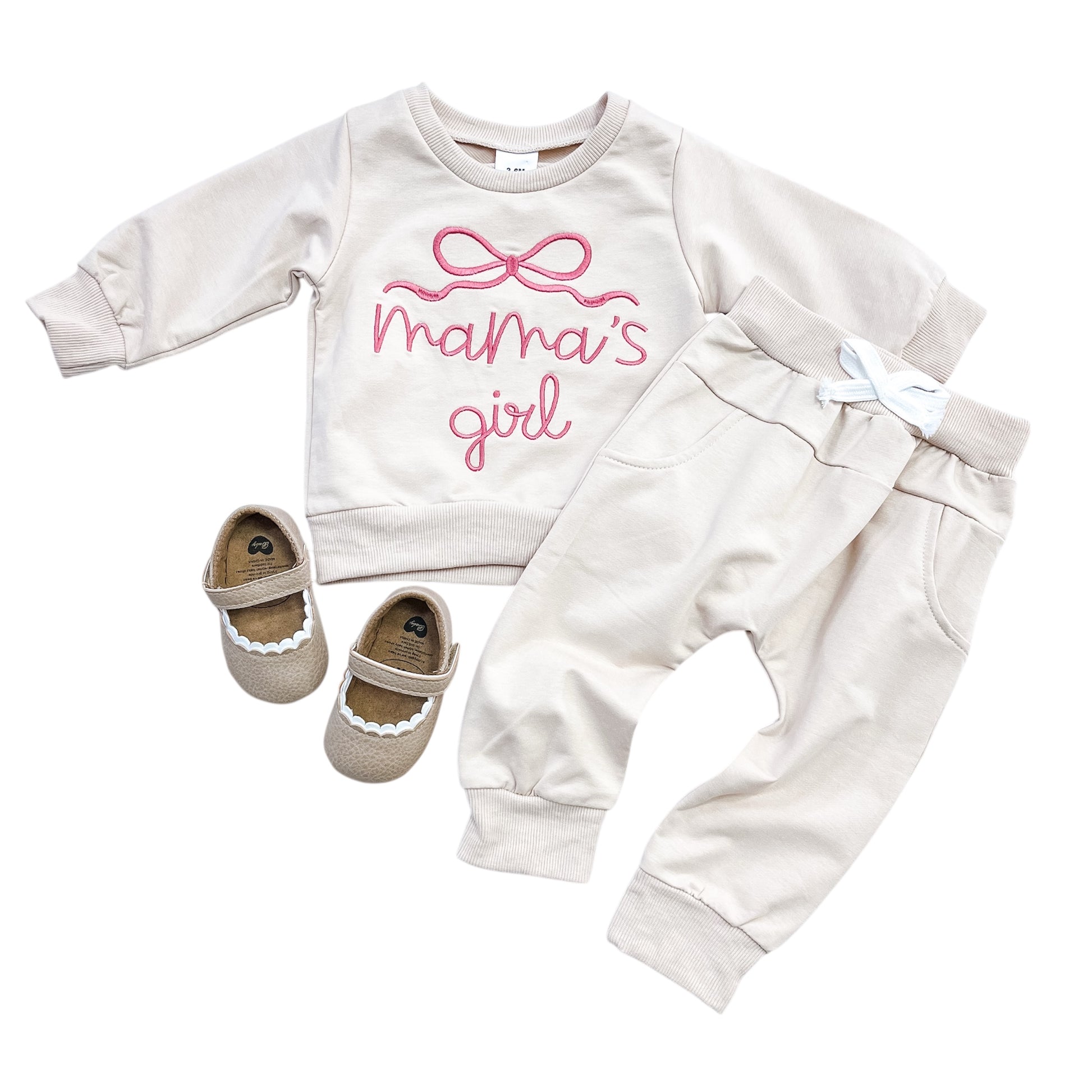 The Tiny Tot Bundles Mama's Girl Cozy Set includes a cream sweatshirt with pink bow and "mama’s girl" text, matching cream joggers with a white drawstring, and brown baby shoes with white trim.