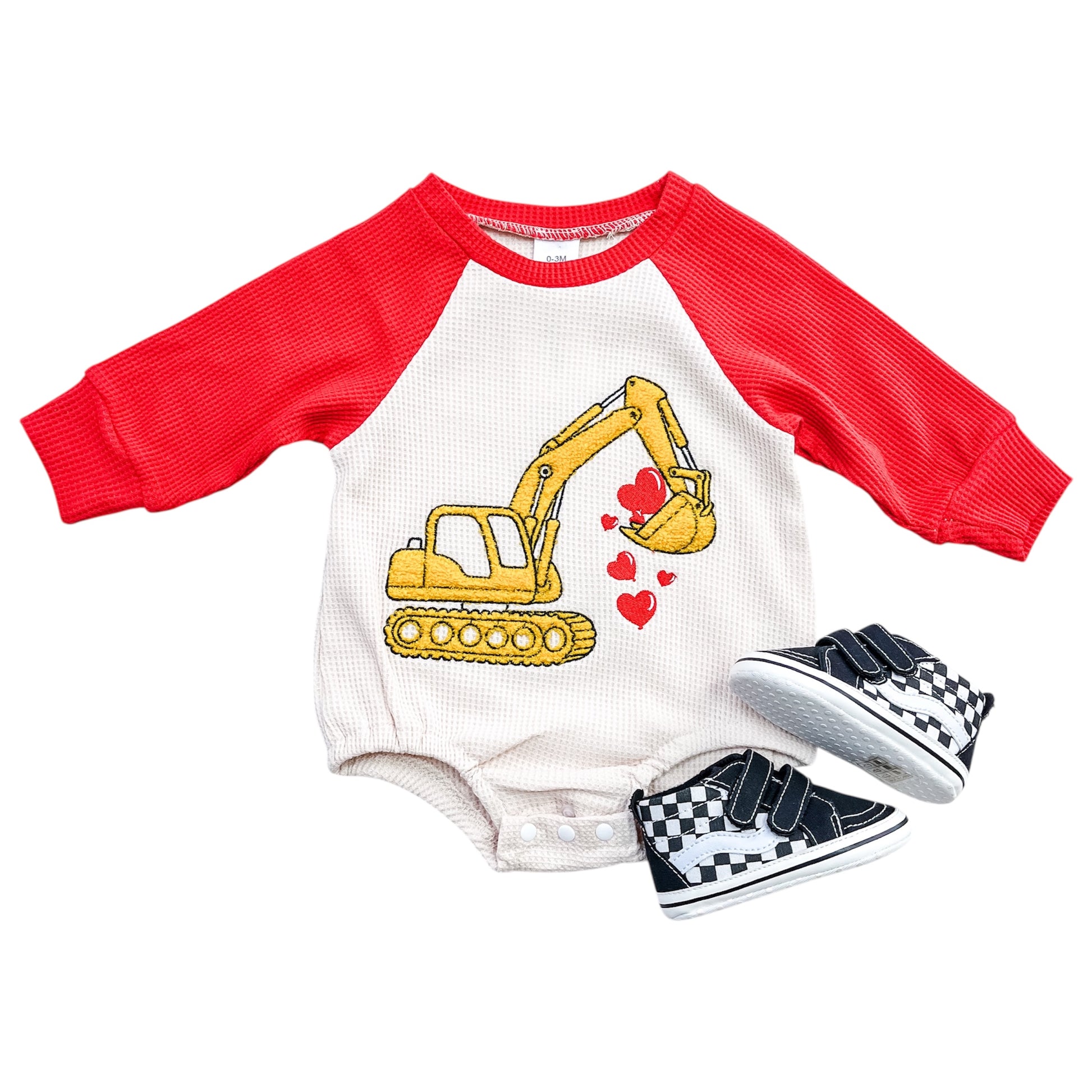 The Tiny Tot Bundles Digger Of My Heart Romper, featuring red sleeves and a yellow excavator scooping red hearts, is shown next to black-and-white checkered baby sneakers.