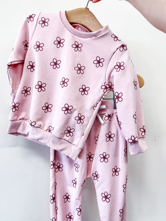 The Blossom Lounge Set by Tiny Tot Bundles features a pink long-sleeve top and pants with a dark pink flower pattern, displayed on a wooden hanger against a white background.