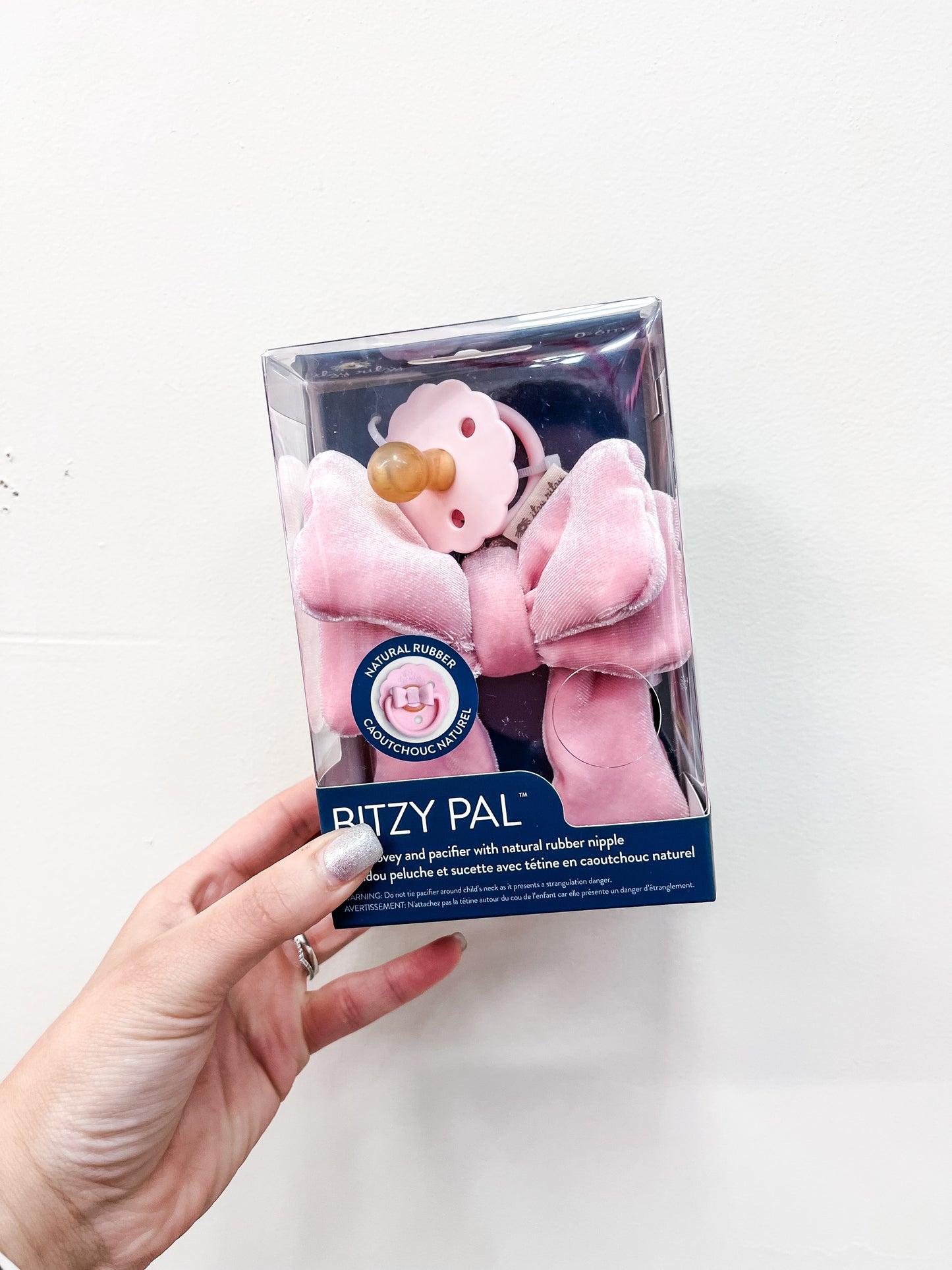 A hand holds a boxed itzy ritzy Velvet Bow Paci Clip against a plain white background.