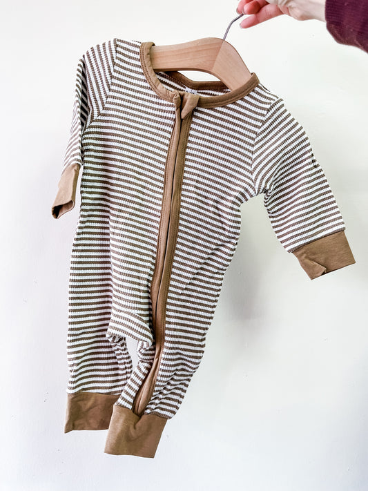 A hand holds the Tiny Tot Bundles Cocoa Stripe Zip Romper—a brown and white striped baby onesie with a front zipper, brown cuffs, and trim—against a plain white background.
