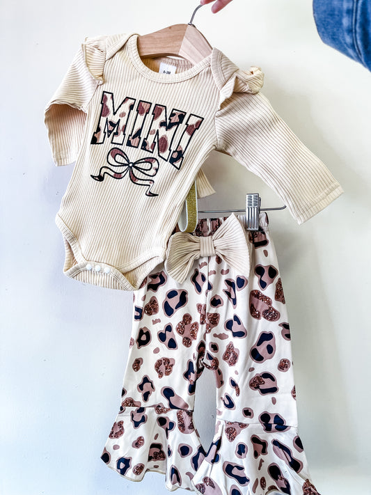 The Leopard Bow Mini Set by Tiny Tot Bundles features a cream long-sleeve onesie with "MINI" in bold, patterned letters, paired with ruffle-bottom pants in a brown and pink leopard print.