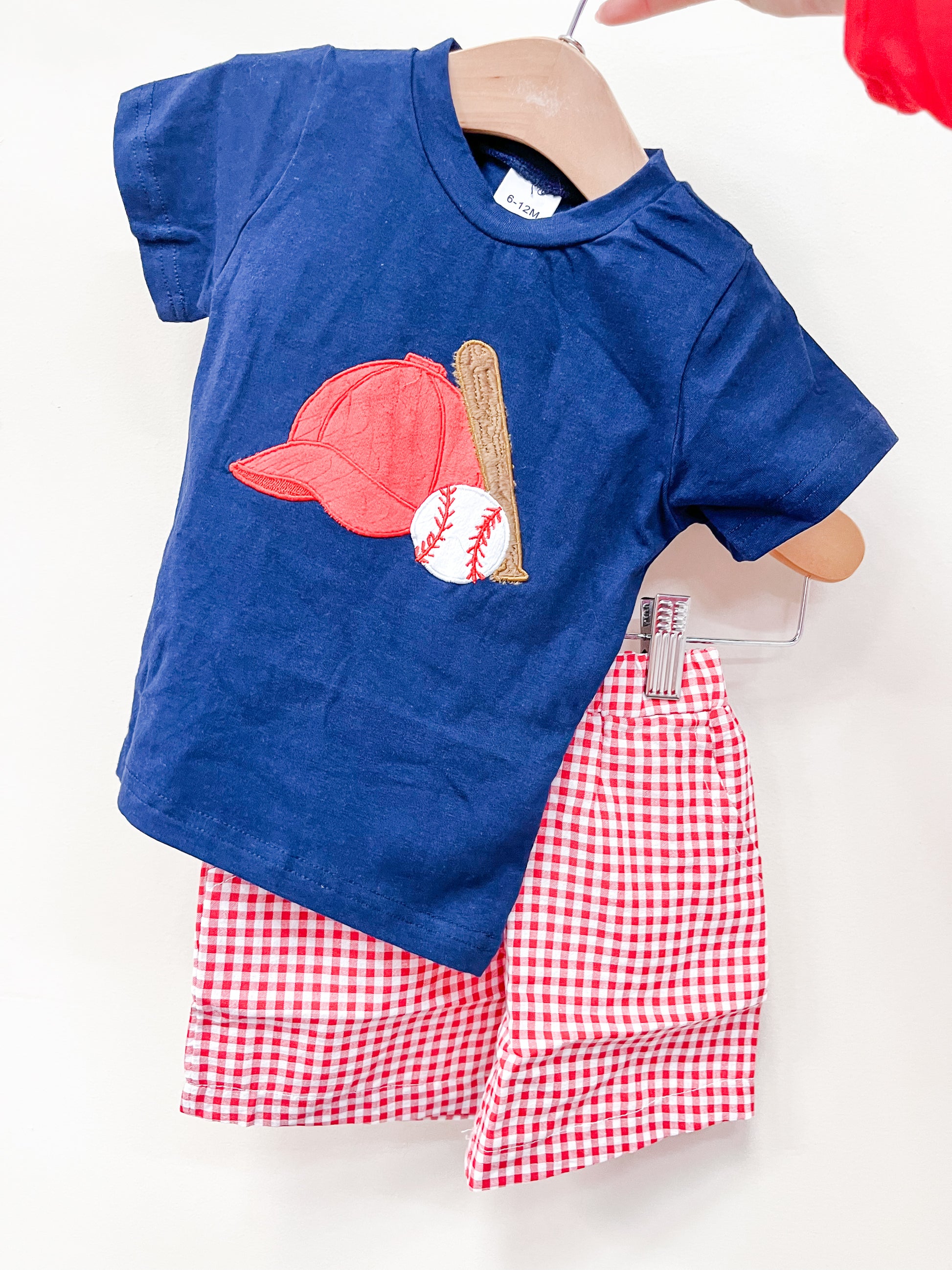 The Baseball Red Gingham Set by Tiny Tot Bundles features a navy blue t-shirt with a red baseball cap, bat, and baseball appliqué, paired with red and white gingham shorts.