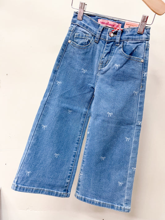 Cutie Patootie’s Bow Babe Denim Jeans feature a wide-leg cut, two front pockets, belt loops, and scattered white bow embroidery. Displayed on a hanger against a white background.