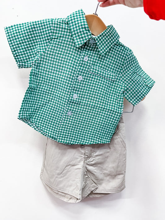 The Gentleman Green Set by Tiny Tot Bundles, featuring a green and white checkered short-sleeve shirt with light beige shorts, is shown on a small hanger held by hand against a plain white background.