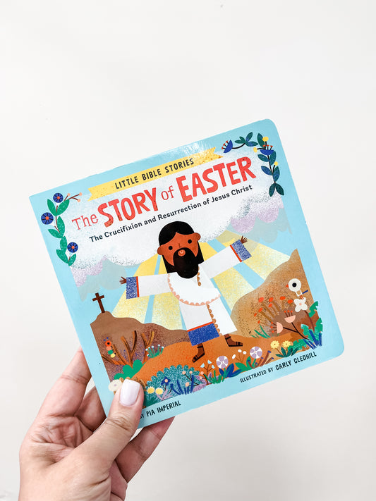 A hand holds "Little Bible Stories: Easter Book" by Tiny Tot Bundles, a colorful children’s book featuring an illustrated Jesus with open arms, flowers, and a cross in the background.