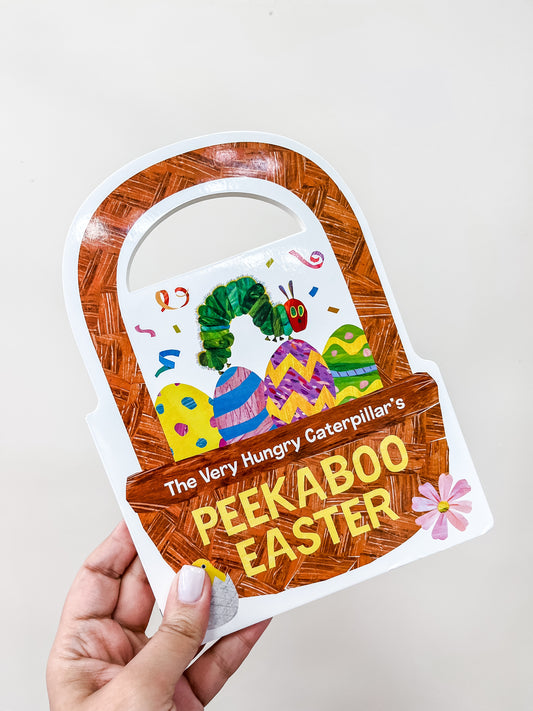 A hand holds the Peekaboo Easter Book by Tiny Tot Bundles, shaped like an Easter basket and featuring The Very Hungry Caterpillar with colorful eggs, confetti, and the title "Peekaboo Easter!" in bold yellow letters.