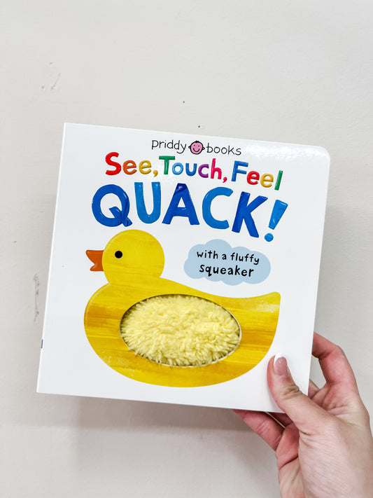 A hand holds the See, Touch, Feel: Quack! Book by Macmillan Publishers, featuring a yellow duck with a textured, fluffy belly patch and a note saying “with a fluffy Squeaker.”.