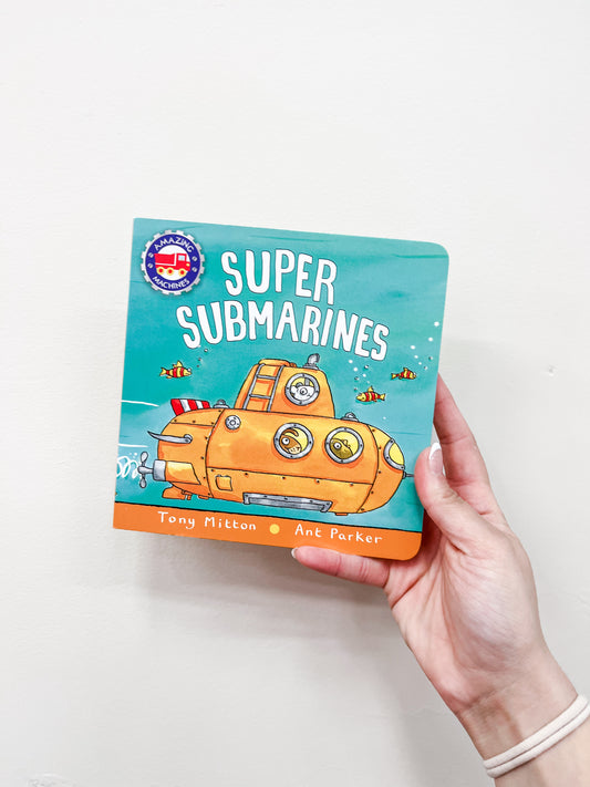 A hand holds the Super Submarines Book by Macmillan Publishers, showing an illustrated yellow submarine and small fish on a blue cover.